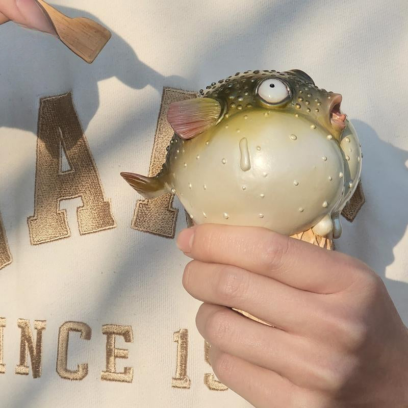 A highly detailed pufferfish ice cream figurine featuring a realistic fish with bulging eyes and textured scales, sitting on an intricately sculpted ice cream cone base. Made of premium resin, this collectible novelty item is perfect for unique decor lovers and marine life enthusiasts.
