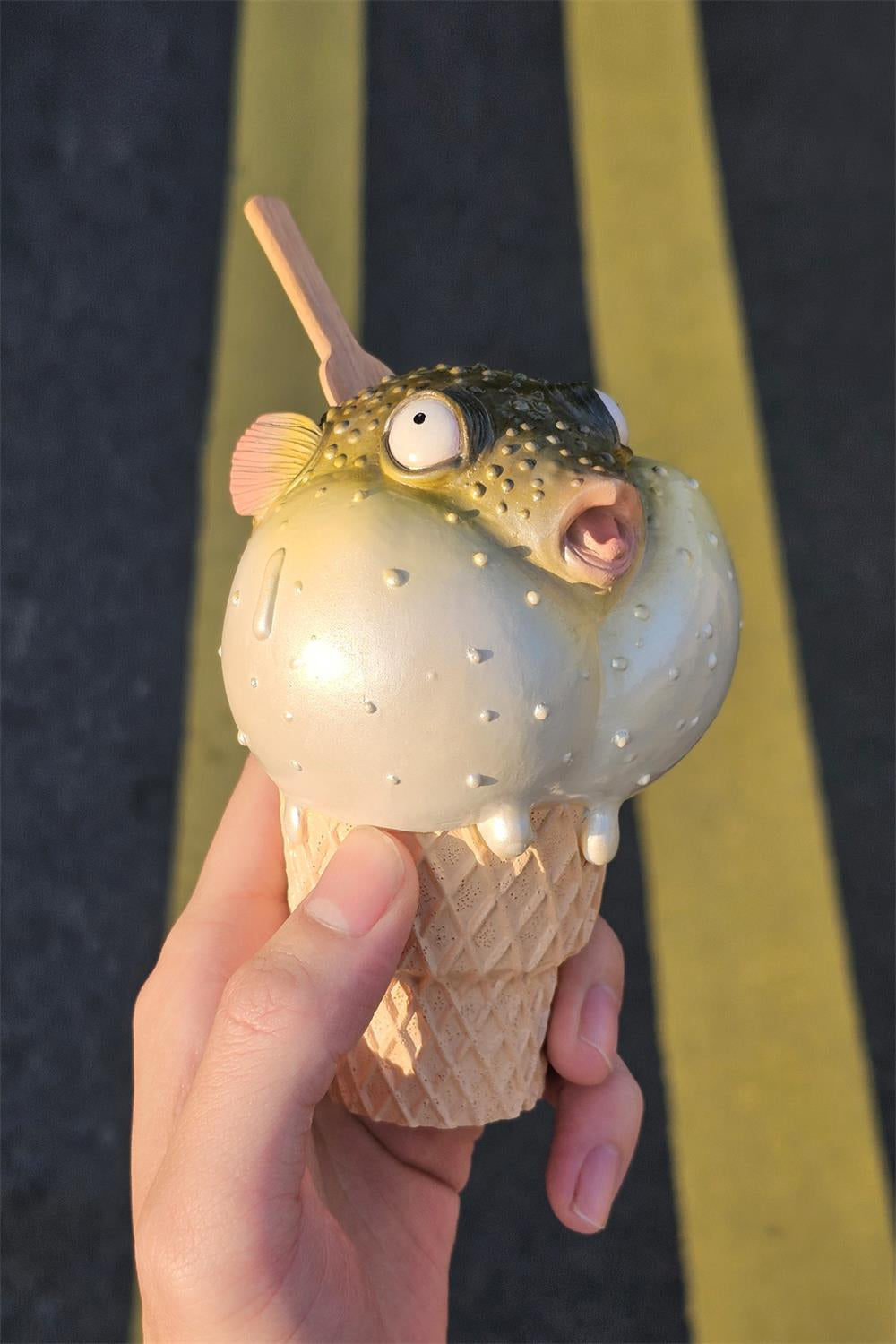 A highly detailed pufferfish ice cream figurine featuring a realistic fish with bulging eyes and textured scales, sitting on an intricately sculpted ice cream cone base. Made of premium resin, this collectible novelty item is perfect for unique decor lovers and marine life enthusiasts.