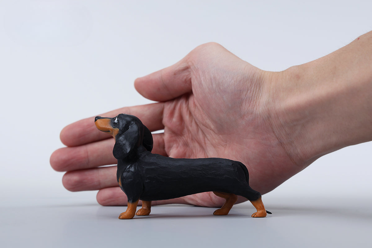 Two small clay Dachshund dog models, one black and one brown, captured in a realistic and lifelike manner. The models showcase detailed features, including expressive eyes and realistic fur textures. Perfect for collectors and dog enthusiasts.