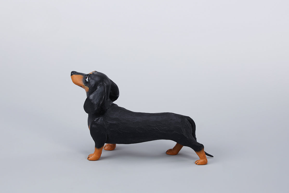 Two small clay Dachshund dog models, one black and one brown, captured in a realistic and lifelike manner. The models showcase detailed features, including expressive eyes and realistic fur textures. Perfect for collectors and dog enthusiasts.