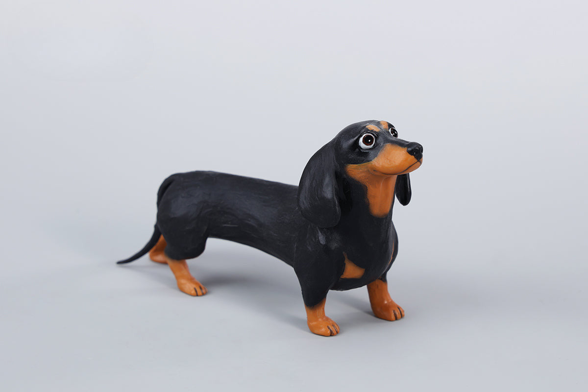 Two small clay Dachshund dog models, one black and one brown, captured in a realistic and lifelike manner. The models showcase detailed features, including expressive eyes and realistic fur textures. Perfect for collectors and dog enthusiasts.