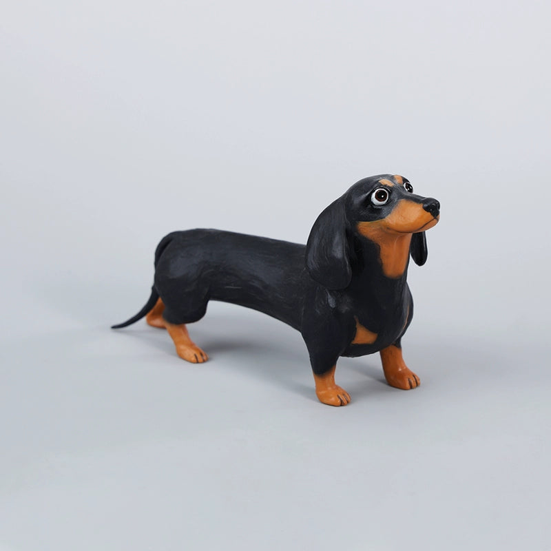 Two small clay Dachshund dog models, one black and one brown, captured in a realistic and lifelike manner. The models showcase detailed features, including expressive eyes and realistic fur textures. Perfect for collectors and dog enthusiasts.