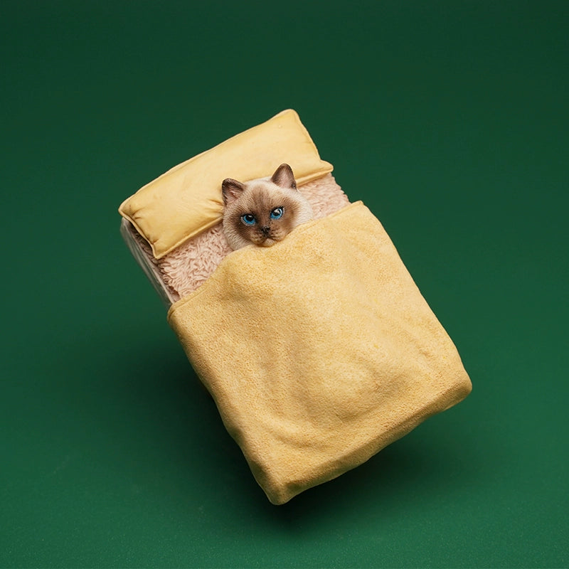 A charming miniature cat figurine tucked under a yellow blanket, lying on a cozy bed with a yellow pillow. The cat's realistic features and expressive eyes make it a delightful collectible for cat lovers and figurine enthusiasts alike.