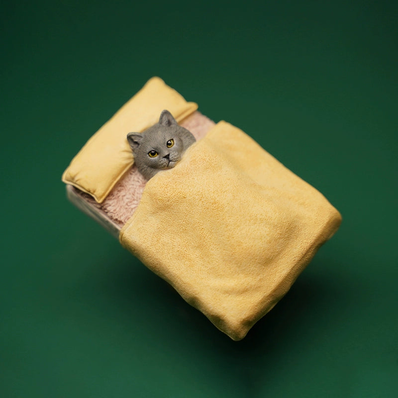 A charming miniature cat figurine tucked under a yellow blanket, lying on a cozy bed with a yellow pillow. The cat's realistic features and expressive eyes make it a delightful collectible for cat lovers and figurine enthusiasts alike.