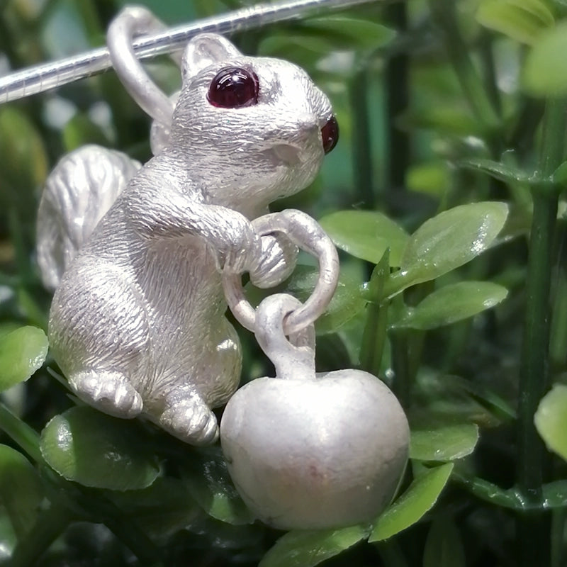 Handcrafted sterling silver squirrel pendant with gemstone eyes, featuring intricate details of a squirrel holding an apple/acorn, available in customizable eye colors. Ideal for personalized gifts and nature lovers, reflecting unique artisanal craftsmanship.