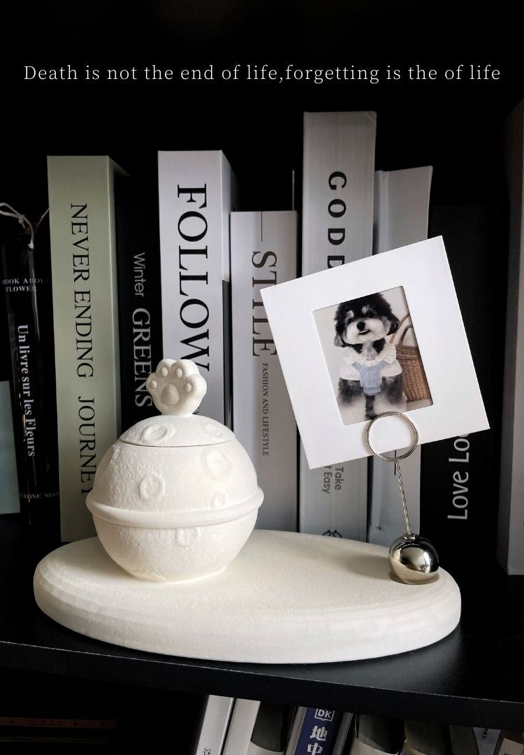 This white moon paw ceramic pet urn features a unique moon-shaped design with a paw print lid and detachable photo frame, measuring 22cm wide and 8cm tall with a 1-2cm base, holding 250ml of ashes. Perfect for North American pet owners honoring small pets like cats or dogs, it offers secure storage and a personalized memorial display for shelves or tables.