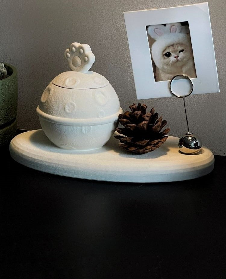 This white moon paw ceramic pet urn features a unique moon-shaped design with a paw print lid and detachable photo frame, measuring 22cm wide and 8cm tall with a 1-2cm base, holding 250ml of ashes. Perfect for North American pet owners honoring small pets like cats or dogs, it offers secure storage and a personalized memorial display for shelves or tables.