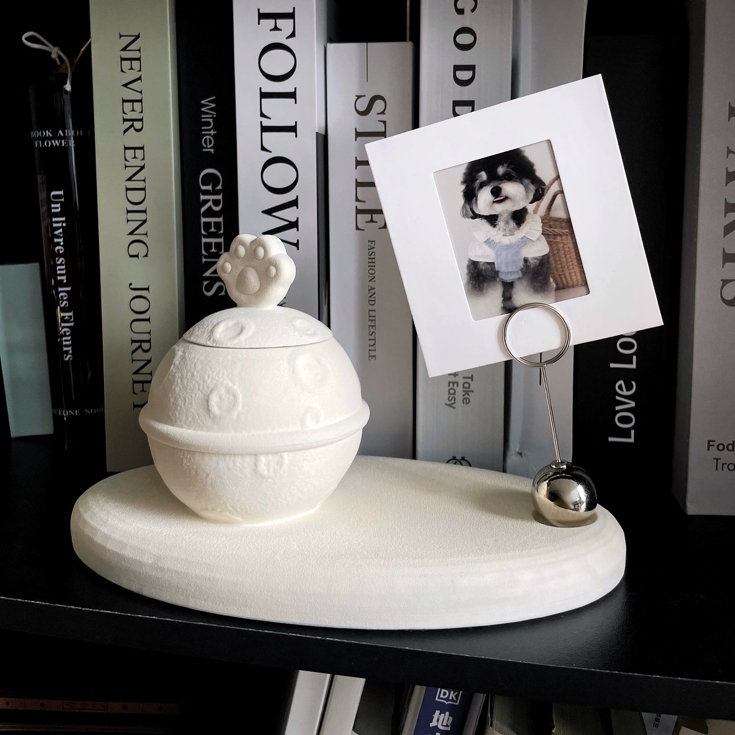 This white moon paw ceramic pet urn features a unique moon-shaped design with a paw print lid and detachable photo frame, measuring 22cm wide and 8cm tall with a 1-2cm base, holding 250ml of ashes. Perfect for North American pet owners honoring small pets like cats or dogs, it offers secure storage and a personalized memorial display for shelves or tables.