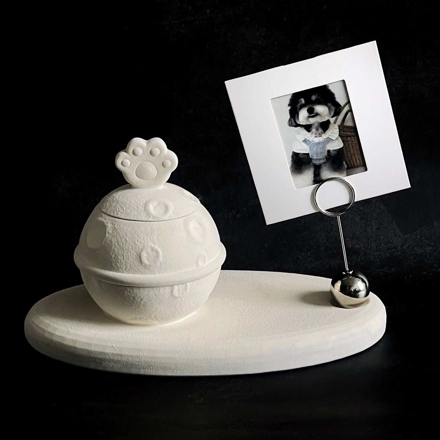 This white moon paw ceramic pet urn features a unique moon-shaped design with a paw print lid and detachable photo frame, measuring 22cm wide and 8cm tall with a 1-2cm base, holding 250ml of ashes. Perfect for North American pet owners honoring small pets like cats or dogs, it offers secure storage and a personalized memorial display for shelves or tables.