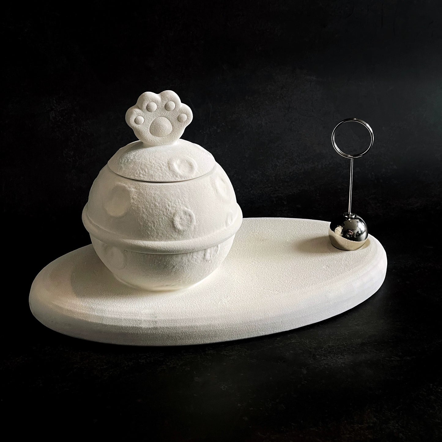 This white moon paw ceramic pet urn features a unique moon-shaped design with a paw print lid and detachable photo frame, measuring 22cm wide and 8cm tall with a 1-2cm base, holding 250ml of ashes. Perfect for North American pet owners honoring small pets like cats or dogs, it offers secure storage and a personalized memorial display for shelves or tables.