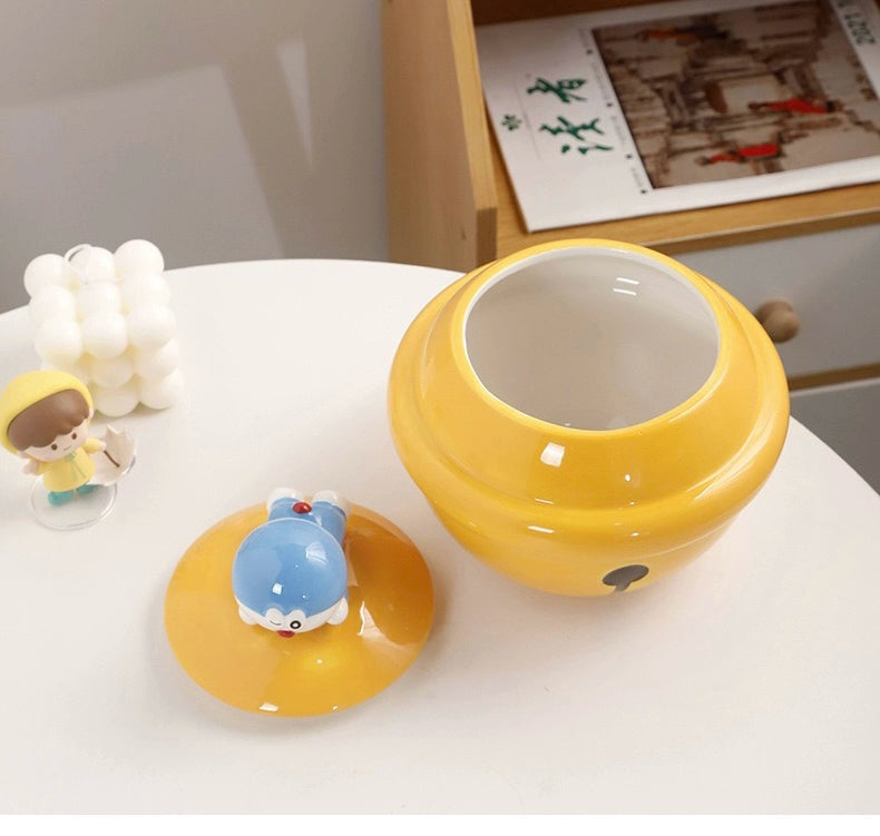 Yellow ceramic Doraemon pet cremation urn with a glossy finish, featuring a round shape and a cute Doraemon figure on top, ideal for North American pet owners. This handcrafted urn provides secure ashes storage, perfect for home memorial display on mantels or shelves, with a vibrant yellow hue and playful design.